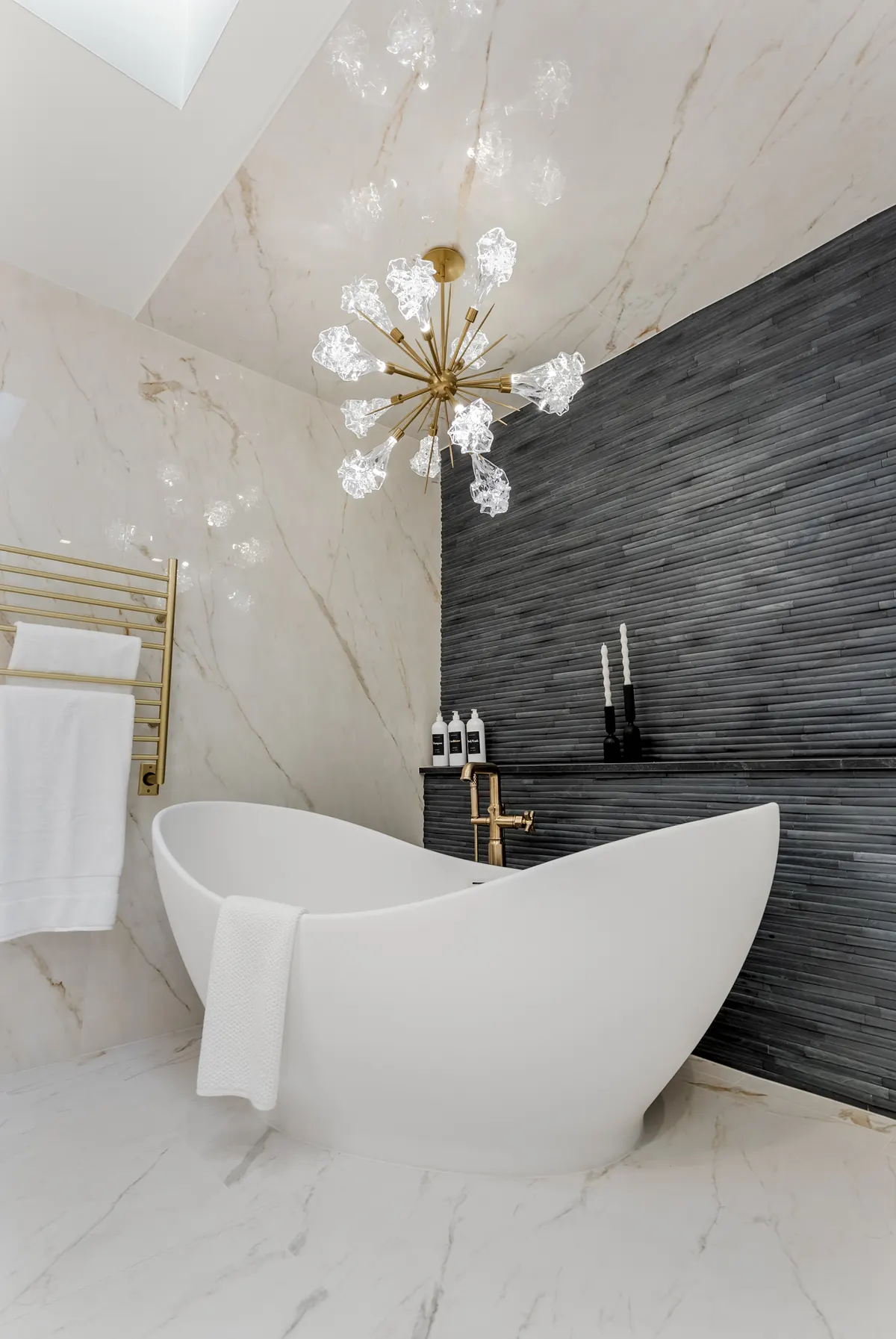 Freestanding tub against a wall of black linear stone tile, with marble-look floors and walls, in a Cherry Hills Village primary bath